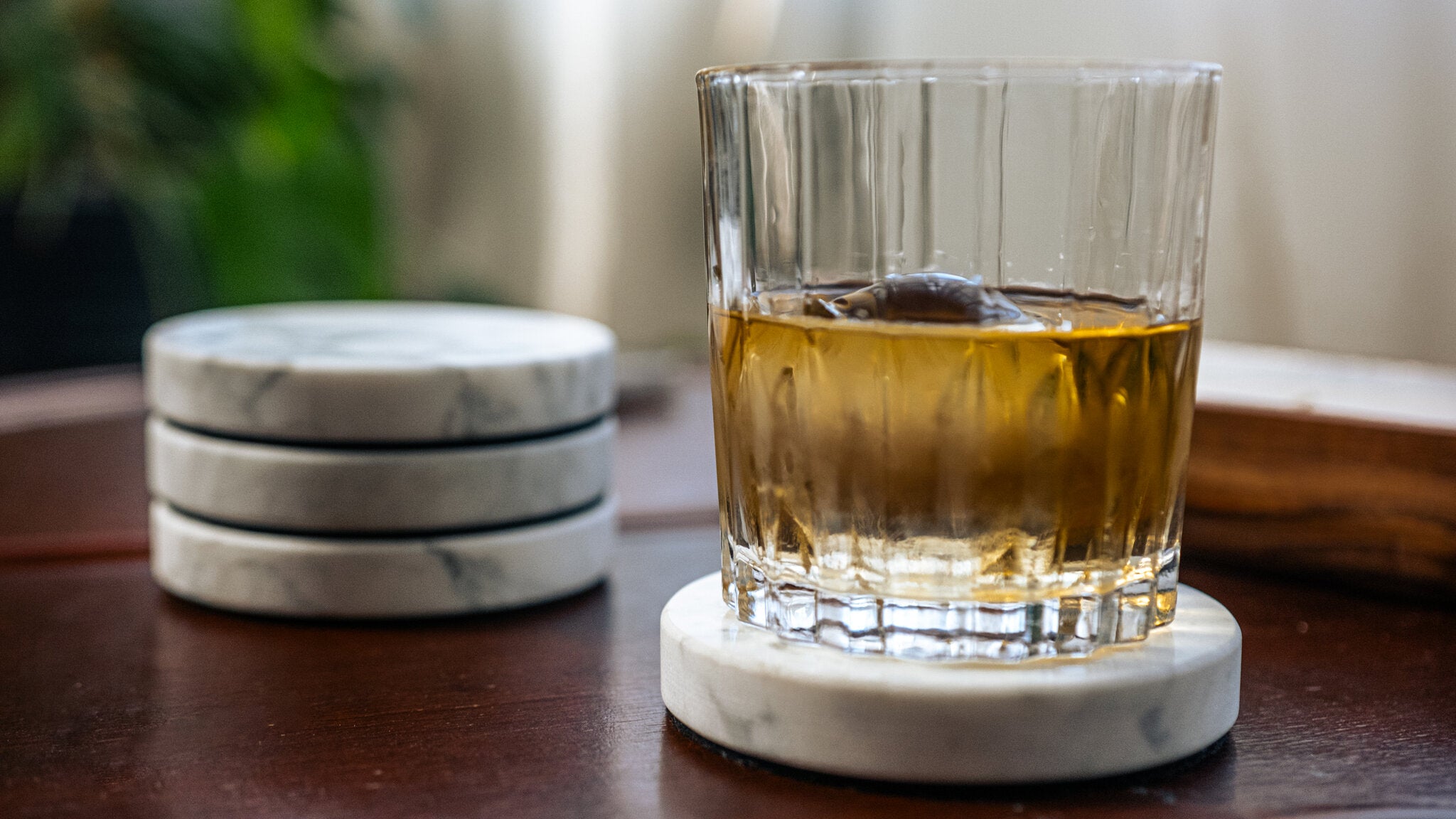 Whiskyglas auf Marmor-Untersetzer mit gestapeltem Set auf dunklem Holztisch